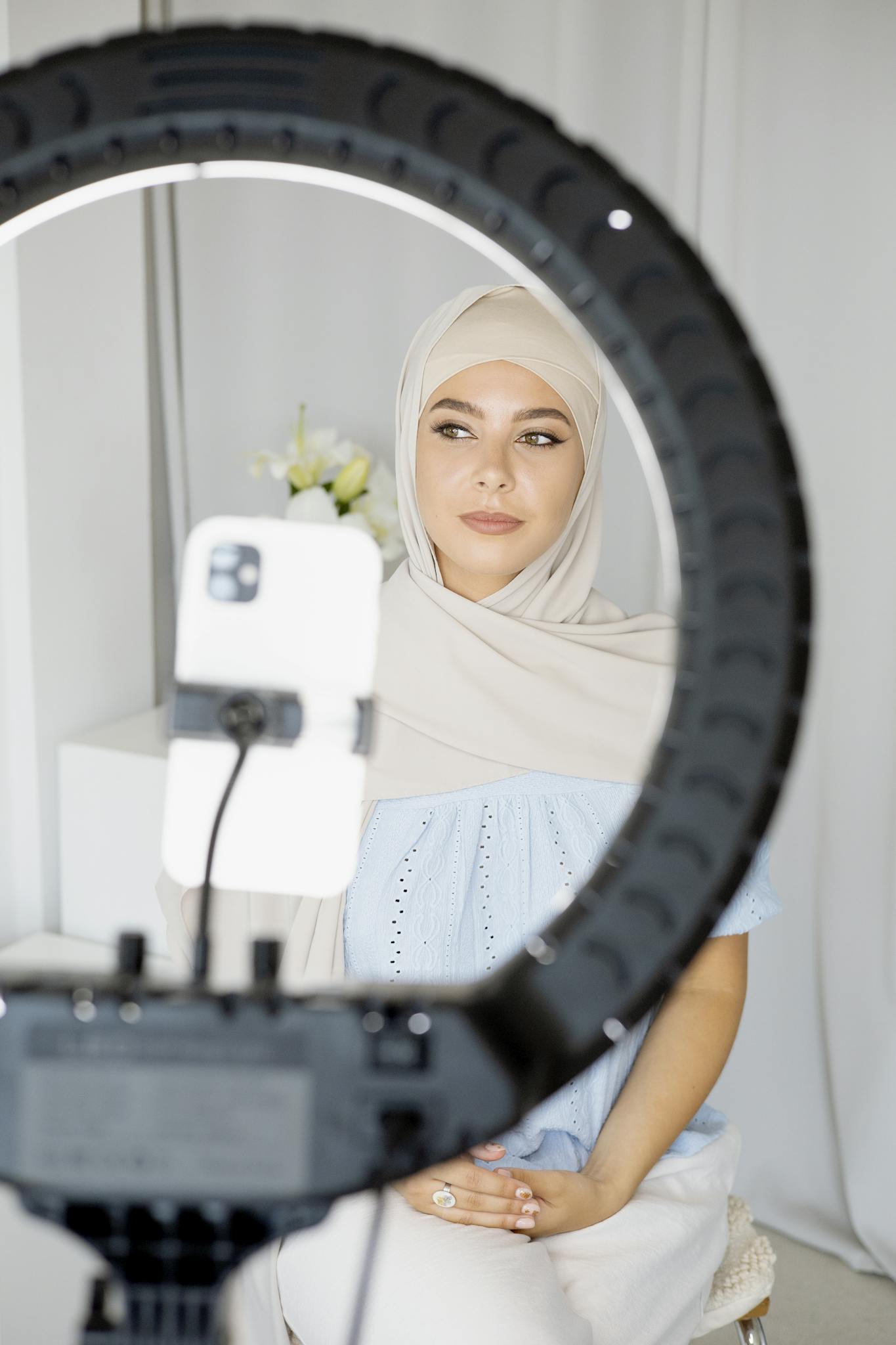 Young Muslim woman vlogging indoors using smartphone and ring light.